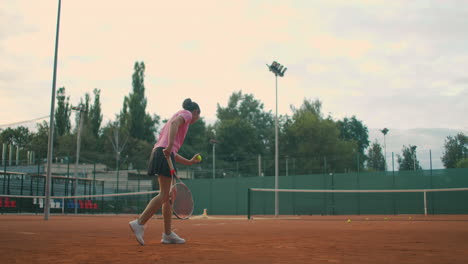 Slow-Motion-commercial-footage-of-tennis-practice-through-the-tennis-court-net.-Straight-view-of-a-female-athlete-playing-the-tennis-game.-A-teenage-sportsman-is-hitting-the-ball-during-sport-training